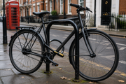 a used city bike secured with a chunky D-lock to a fixed cycle stand on a UK street