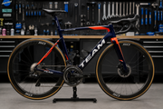 A used road bike in team livery photographed side-on in a workshop setting, showing race-spec wheels and drivetrain.