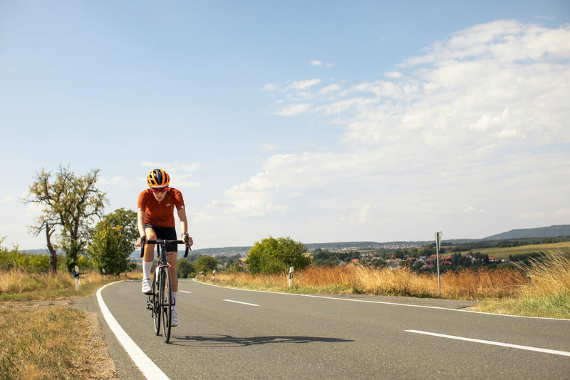 Road cyclist wearing an orange jersey and helmet riding on a country road — imagery for selling used road bikes on MyNextBike.co.uk.