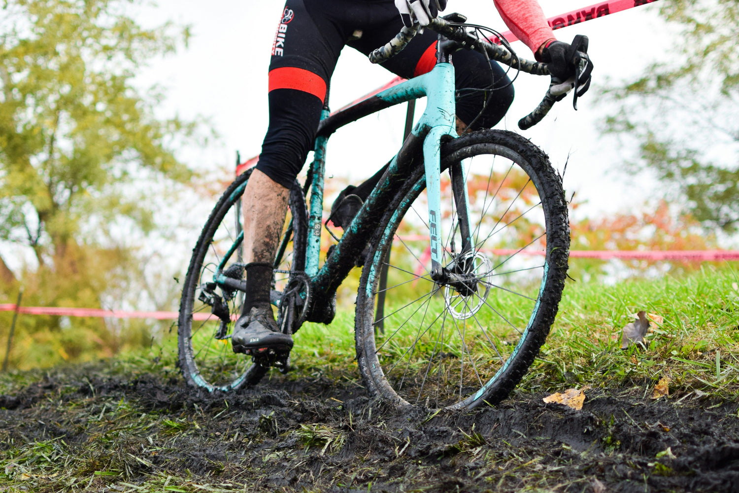 Cyclocross cyclist riding a mud-covered bike through a wet, grassy course — demonstrating the durability and off-road ability of cyclocross bikes often found on second-hand bike marketplaces in the UK like MyNextBike.