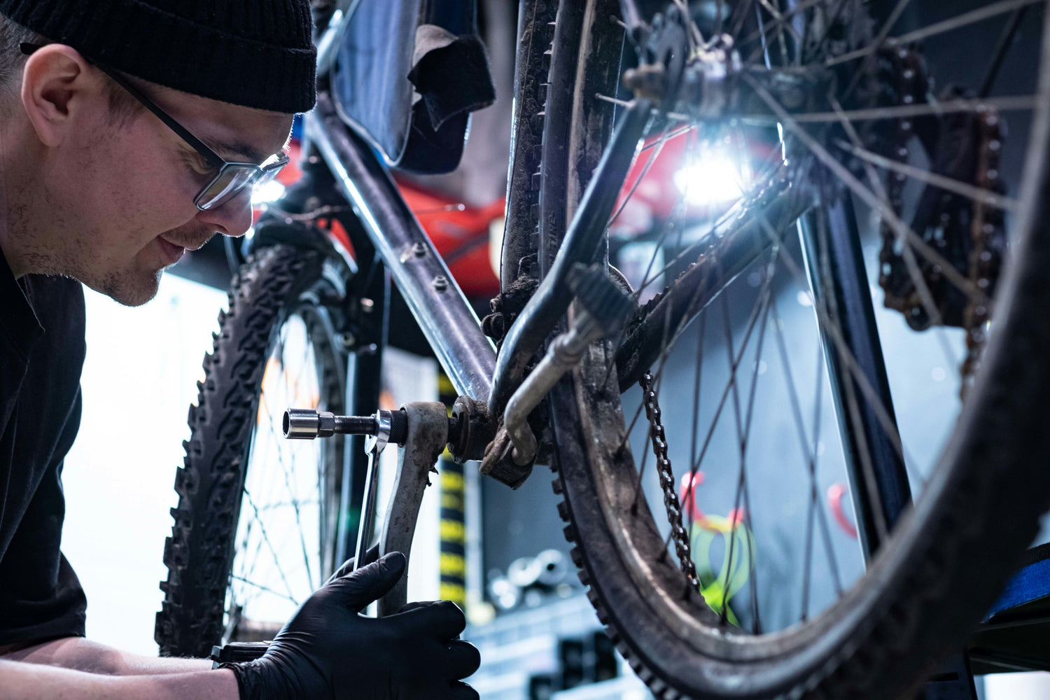 Mechanic inspecting and tightening the crank arm on a used mountain bike during a condition check — assessing frame, tyres, and drivetrain for resale on MyNextBike.co.uk. 