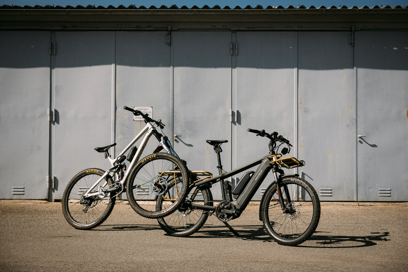 Two modern bicycles, including an electric bike, parked outside a building at a community bike sale, showcasing second-hand bikes ready for resale.