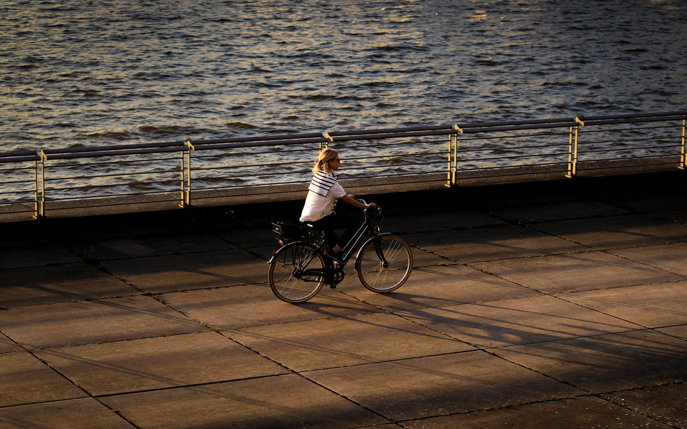 Woman riding a second-hand hybrid bike along a riverside path in the UK at sunset – get your next pre-loved women’s bike from MyNextBike.co.uk 