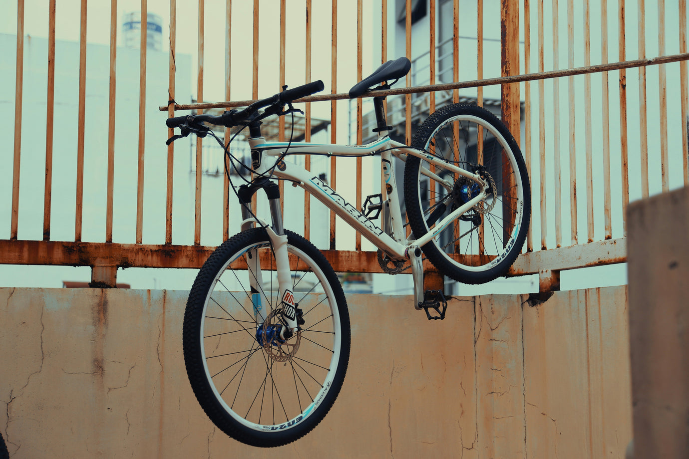 Used hardtail mountain bike leaning against an urban metal fence, showing suspension fork, disc brakes, and trail-ready tyres