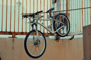 Used hardtail mountain bike leaning against an urban metal fence, showing suspension fork, disc brakes, and trail-ready tyres