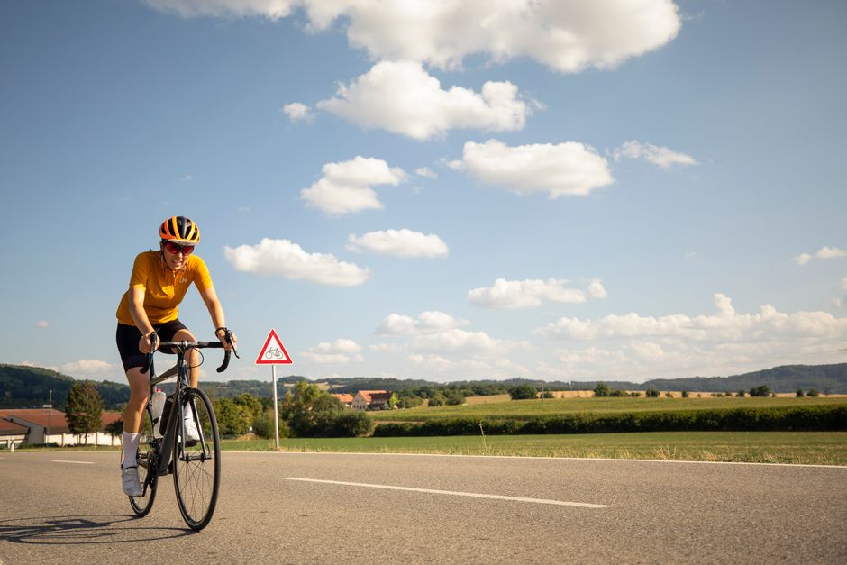 A cyclist in yellow rides a road bike on a sunny day with a beautiful countryside backdrop.