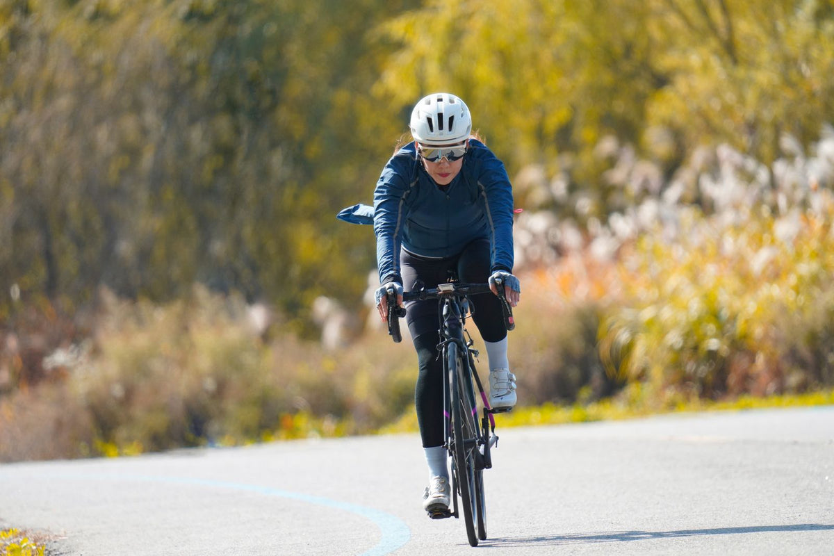 Woman in a helmet riding a black drop-bar road bike along a paved path in autumn