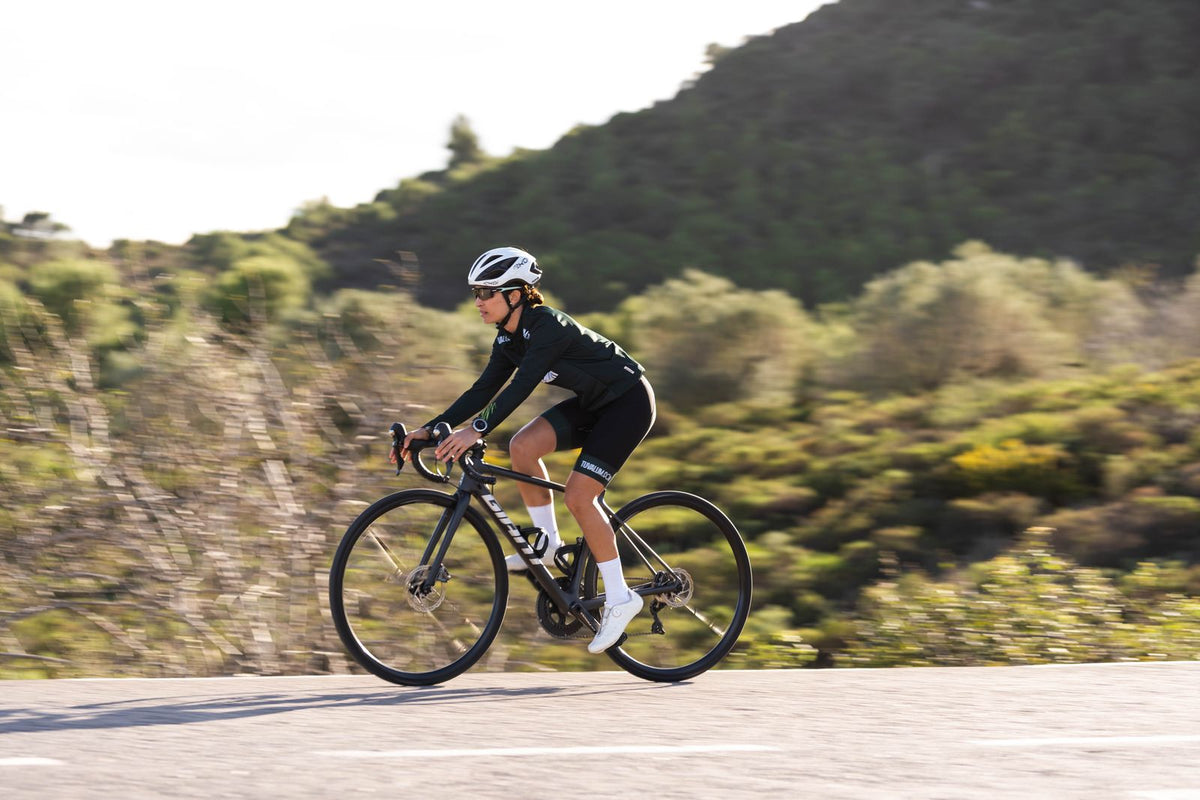 Woman in a helmet riding a black drop-bar road bike along a country road