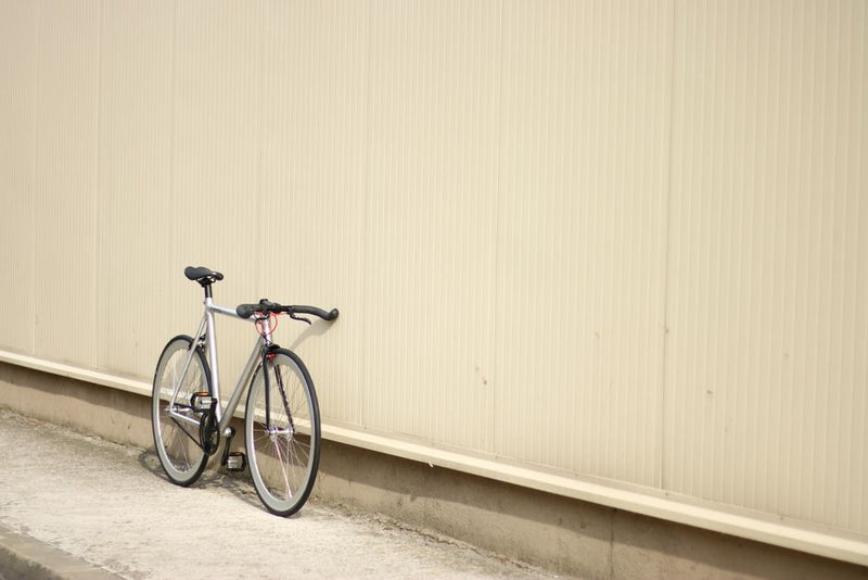 A lone bicycle leans against a minimalist beige wall in an urban setting, depicting simplicity.