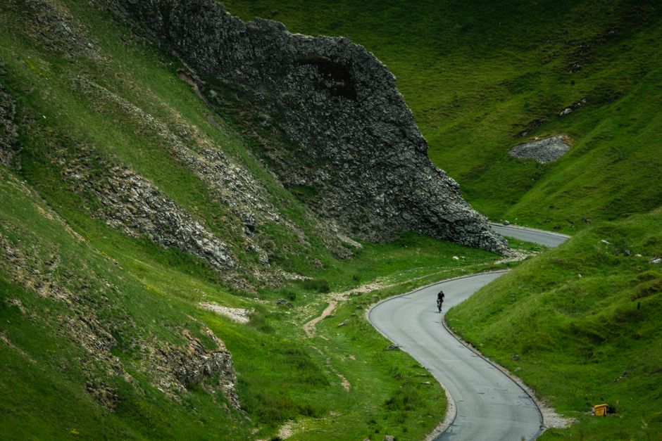 Cyclist riding on a winding road through lush green mountains in the English countryside.