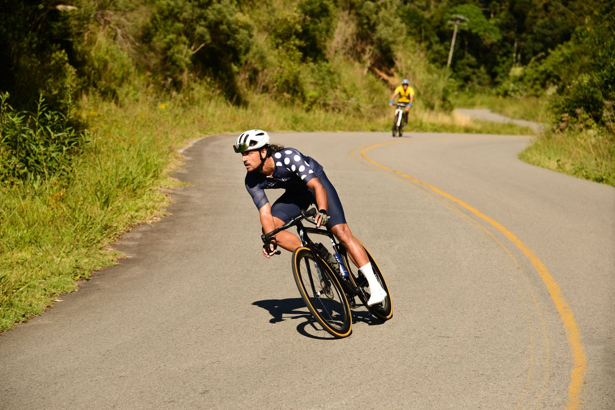 Road cyclist leaning through a bend on a country road, with a second rider in the background