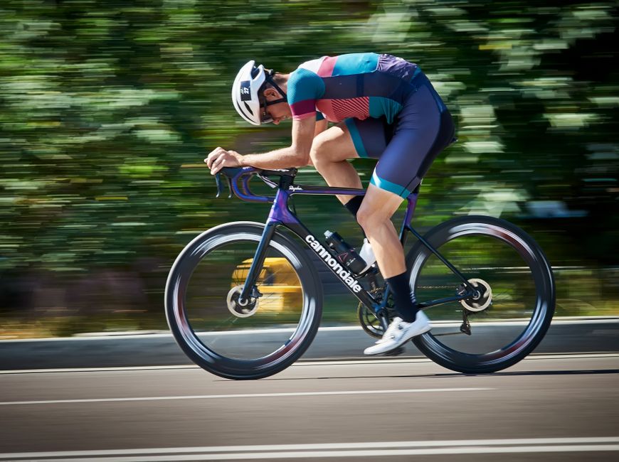 Full body side view of sportsman cycling bike on asphalt road near green trees during training in park