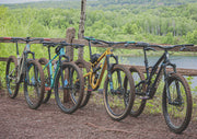 Hardtail vs full suspension mountain bikes lined up on a woodland trail, comparing mountain bike suspension styles for trail riding.